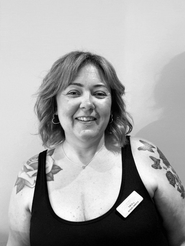 Portrait of a smiling woman with shoulder length hair tattoos on both arms wearing a black tank top and a name badge